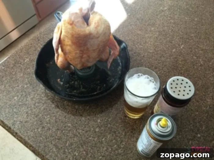 Preparing the best beer can chicken recipe for the barbecue: an easy, flavorful way to cook outdoors in summer. #beercanchicken A raw whole chicken is prepared for beer can chicken by being placed upright on a can in a roasting pan on a kitchen counter, surrounded by a glass of beer, seasoning, and a canister, ready for the charcoal grill.