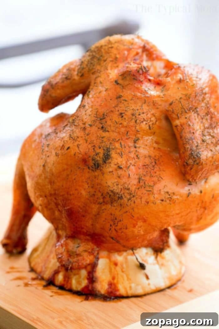 Juicy Beer Can Roast Chicken 3 A close-up shot of a beautifully golden-brown beer can chicken, perfectly cooked on a charcoal grill, with visible seasoning on its crispy skin, showcasing the delicious end result.