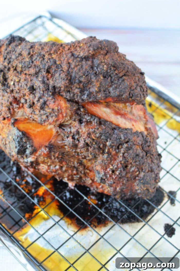 Oven Roasted Pork 4 A large, crispy, blackened Pork Roast in Oven rests on a wire rack over a baking sheet with savory drippings.