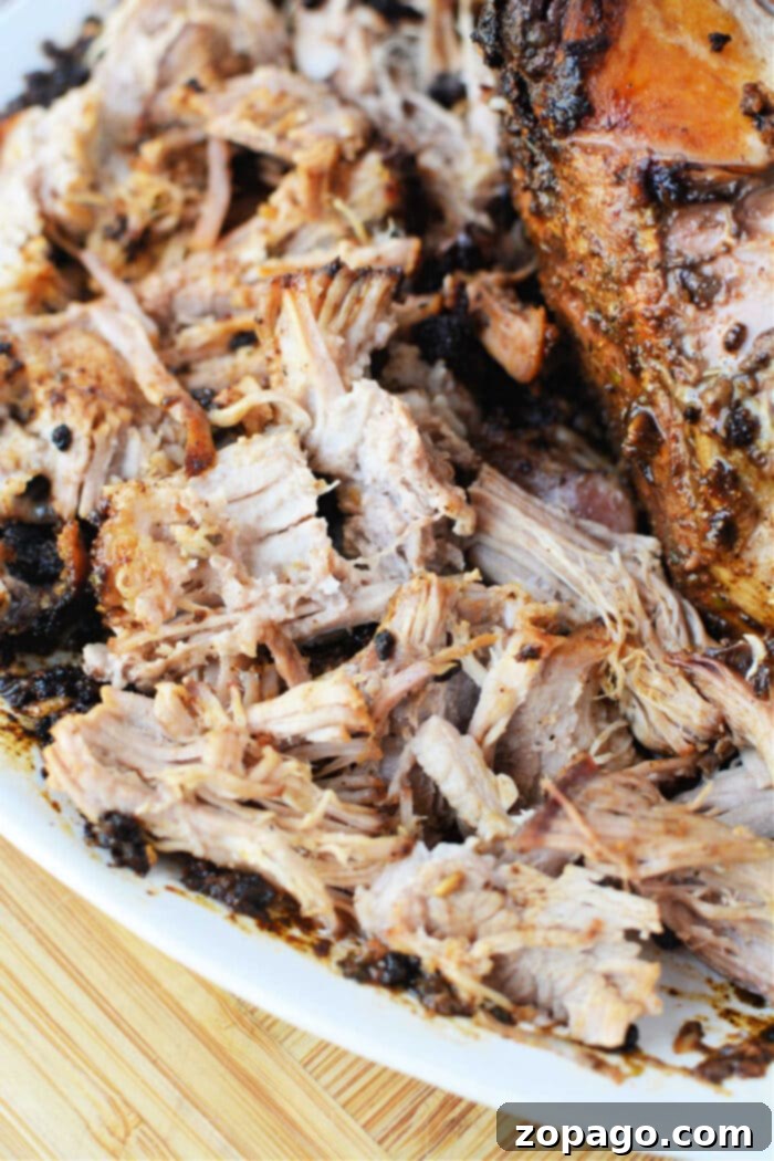 Oven Roasted Pork 5 Shredded, seasoned pork roast on a white plate atop a wooden surface—perfect for showing off your favorite oven pork roast recipe.