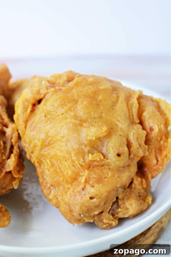 Crispy Skillet Chicken 4 A piece of golden, crispy Pan Fried Chicken thighs sits on a white plate, ready to enjoy.