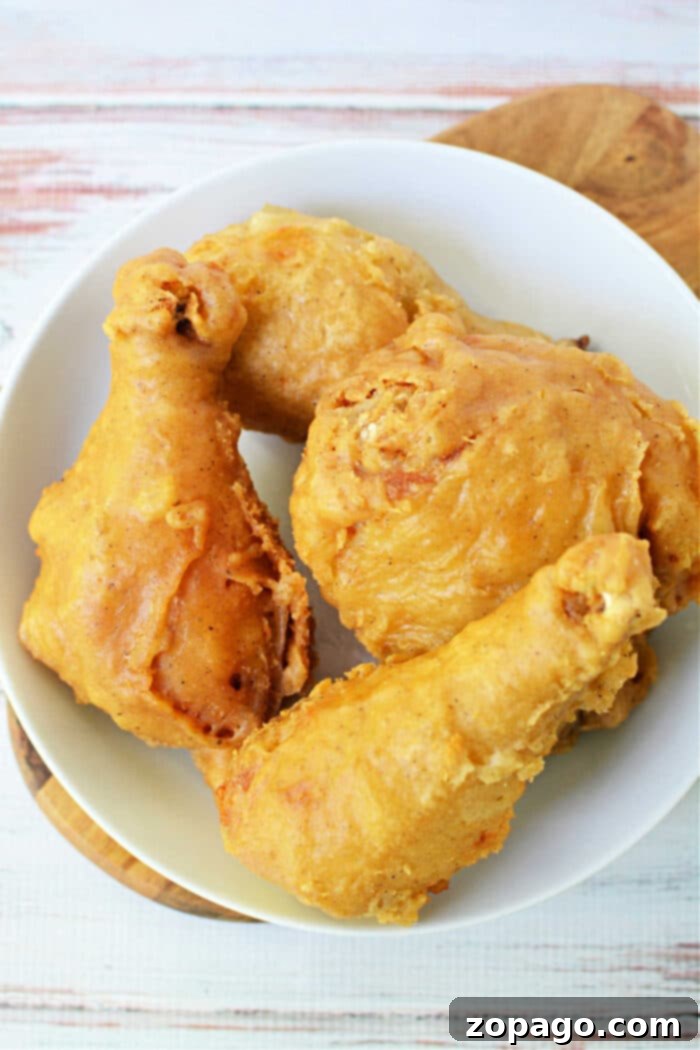 Crispy Skillet Chicken 5 Four pieces of golden, crispy pan fried chicken on a white plate atop a wooden surface.