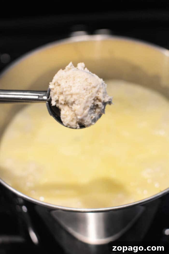 A spoonful of fluffy ricotta curds held over a pot of simmering liquid on a stovetop, beautifully illustrating the comforting warmth and texture reminiscent of classic Bisquick recipes like Chicken and Dumplings.