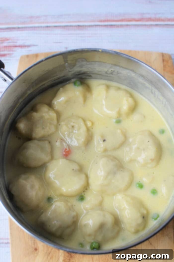 A close-up shot of a pot of creamy chicken and dumplings made with Bisquick, studded with sweet peas and carrots, resting invitingly on a wooden cutting board, ready to serve.