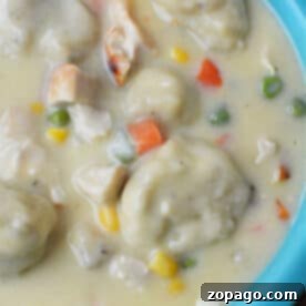 Creamy Chicken and Dumplings soup with vegetables in a blue bowl, made easy with Bisquick for fluffy dumplings—comfort food at its finest.