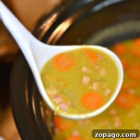A ladle of comforting slow cooker split pea soup with ham and carrots overflows the crockpot, highlighting a hearty and easy meal.