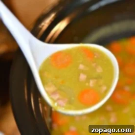 A ladle of slow cooker split pea soup with ham and carrots overflows the crockpot, showcasing a delicious and easy slow cooker soup recipe.