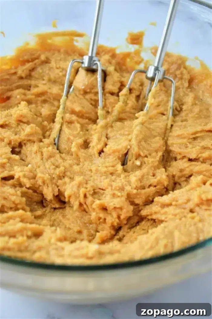 Golden Peanut Butter Thumbprints 4 An electric hand mixer blending yellowish-orange batter in a glass bowl, perfect for 3 ingredient peanut butter thumbprint cookies.