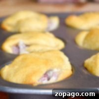 Golden brown ham turnovers, the perfect leftover ham recipe, nestle in a muffin tin on a rustic wooden table.