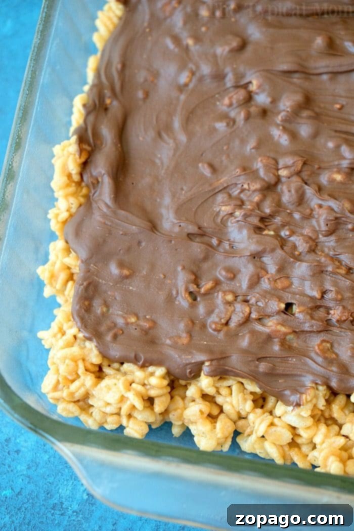 No-bake recipe for Scotcheroos using rice krispies or cheerios and ooey gooey goodness. SO addictive. Preparing no-bake Scotcheroos, showing the peanut butter and butterscotch mixture being pressed into a greased pan with parchment paper.