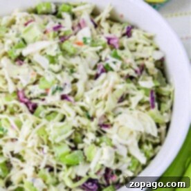 A bowl of fresh coleslaw, perfect for a pulled pork feast, features crisp cabbage, carrots, and green onions, all served beside sliced lemons.