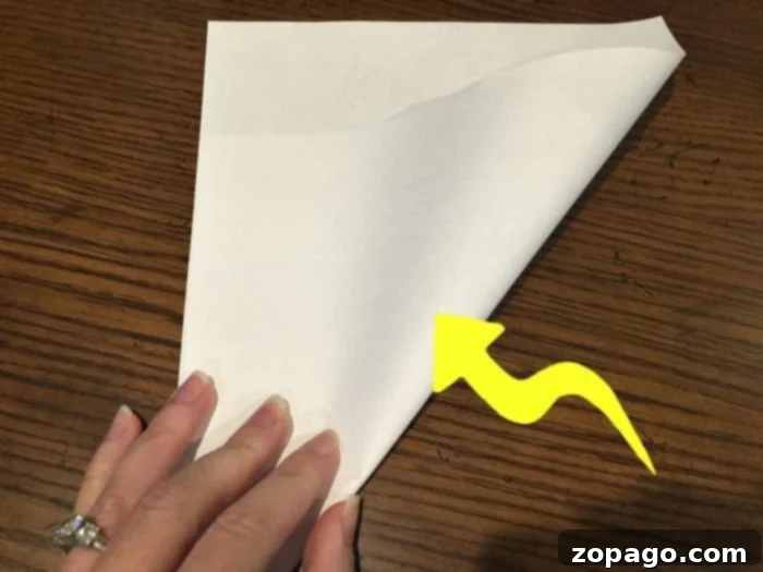 Craft Your Own Fortune Teller 2 Close-up of hands expertly folding a white sheet of paper diagonally, demonstrating the first step in creating a DIY paper fortune teller for math practice.