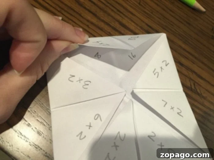 Craft Your Own Paper Fortune Teller 4 An overhead shot demonstrating the final folding steps of a paper fortune teller. The image shows the smaller square being folded in half, revealing the pockets where fingers will be inserted to operate the math facts game.