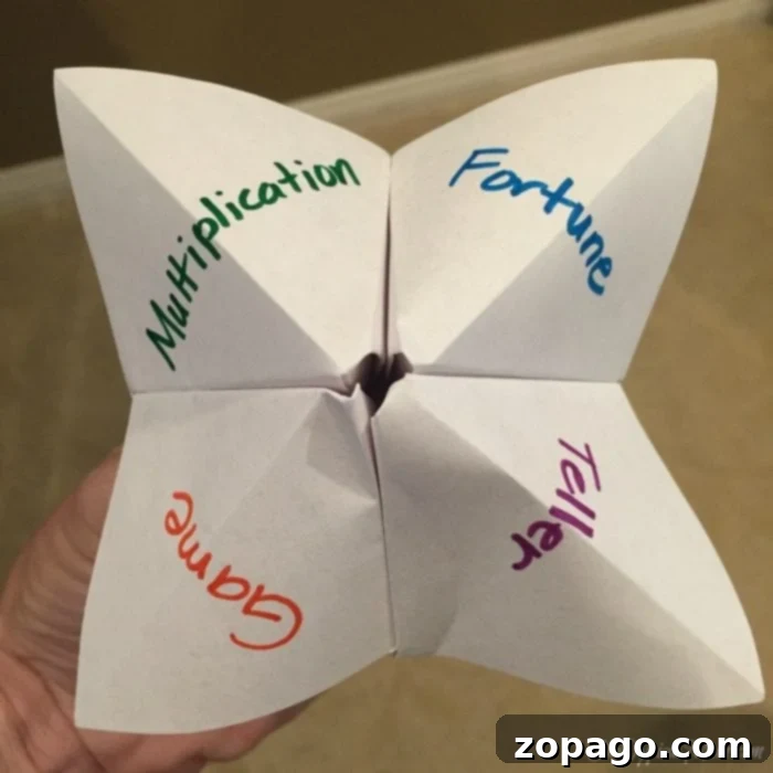 Craft Your Own Paper Fortune Teller 5 A child's hand operating a completed paper fortune teller, clearly showing multiplication problems written on the inner flaps and answers concealed underneath. The fortune teller is a fun math facts game designed for interactive learning.