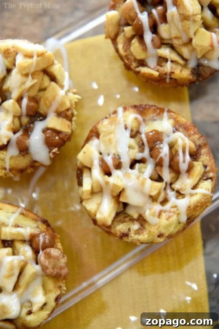 Tiny Temptation Apple Pies 6 A close-up of four caramel apple cinnamon rolls on a yellow napkin. The rolls, reminiscent of a recipe for mini apple pies, are topped with chopped apples, caramel bits, and drizzled with white icing. The rolls appear golden brown and are arranged on a clear tray.