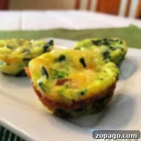 Three spinach and cheese egg muffins, reminiscent of a crustless spinach quiche, rest on a white plate atop a green placemat with a blurred background.