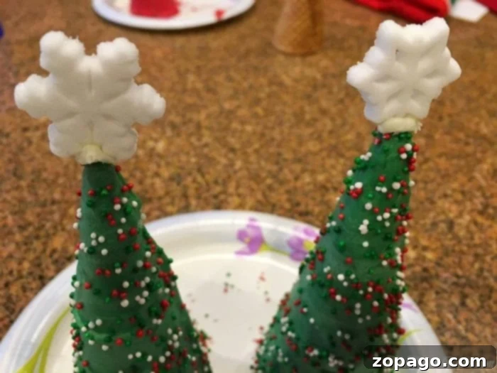 A fun holiday craft for kids: decorating edible Christmas trees with sprinkles. Child's hands decorating a Christmas tree sugar cone with sprinkles