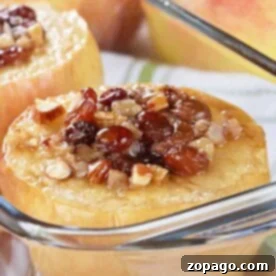 Baked apples filled with nuts and raisins in a glass dish, with fresh apples in the background, provide a delightful guide on how to bake whole apples.