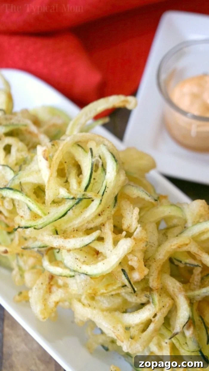 Delicious salt and pepper zucchini chips with a light and crispy tempura batter, perfect as a snack or side. Spiralized zucchini ribbons coated in tempura batter, ready for frying.