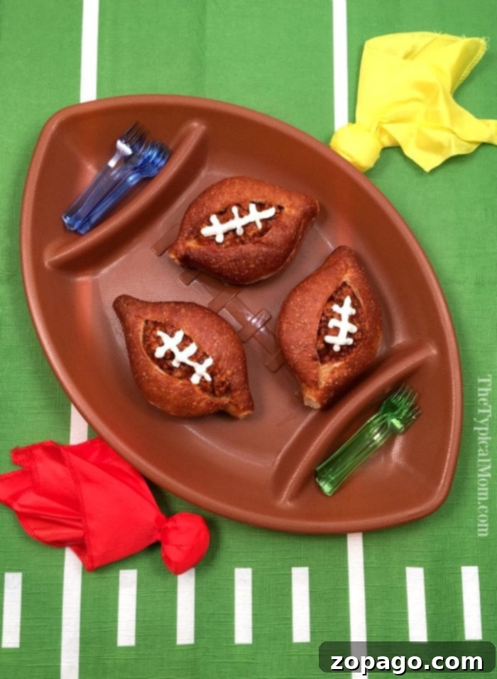 Sloppy Joe bread bowls are great for a football appetizer or any other party you're having! EASY to make and delicious! #football #sloppyjoes #superbowl #appetizer #breadbowls A brown football-shaped platter holds three sloppy joe filled bread bowls with sour cream lacing on the top.