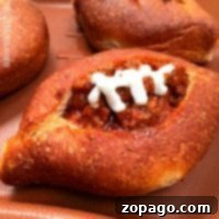 A sloppy joe bread bowl filled with a savory meat and tomato mixture, topped with a zigzag of white dressing resembling football laces, all served on a brown tray.