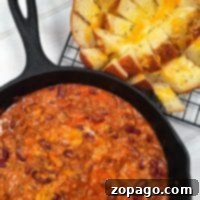 A skillet of cheesy chili with beans sits beside a loaf of pull-apart bread on a cooling rack.