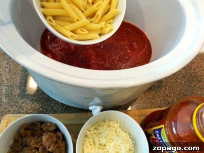 This slow cooker pizza casserole recipe is amazing! So easy to make in your crockpot and great for dinner or a party with kids. #slowcooker #pizza #crockpot #casserole #crockpotrecipes #thetypicalmom Pasta mixing with tomato sauce in a slow cooker, surrounded by bowls of sausage and cheese.