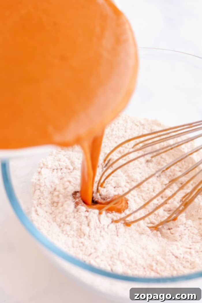 Pumpkin Spice Baked Donuts 4 Pumpkin puree being poured into a bowl of dry ingredients with a whisk, creating the perfect base for baked pumpkin donuts.