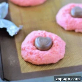 A delightful pink cookie, crafted from a strawberry cake mix, rests with a heart-shaped chocolate atop a baking sheet.