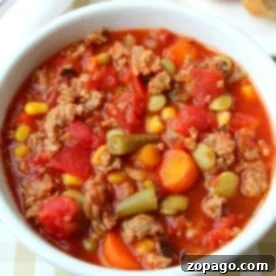 A crock pot full of hearty vegetable beef soup, brimming with corn, carrots, green beans, and tomatoes.