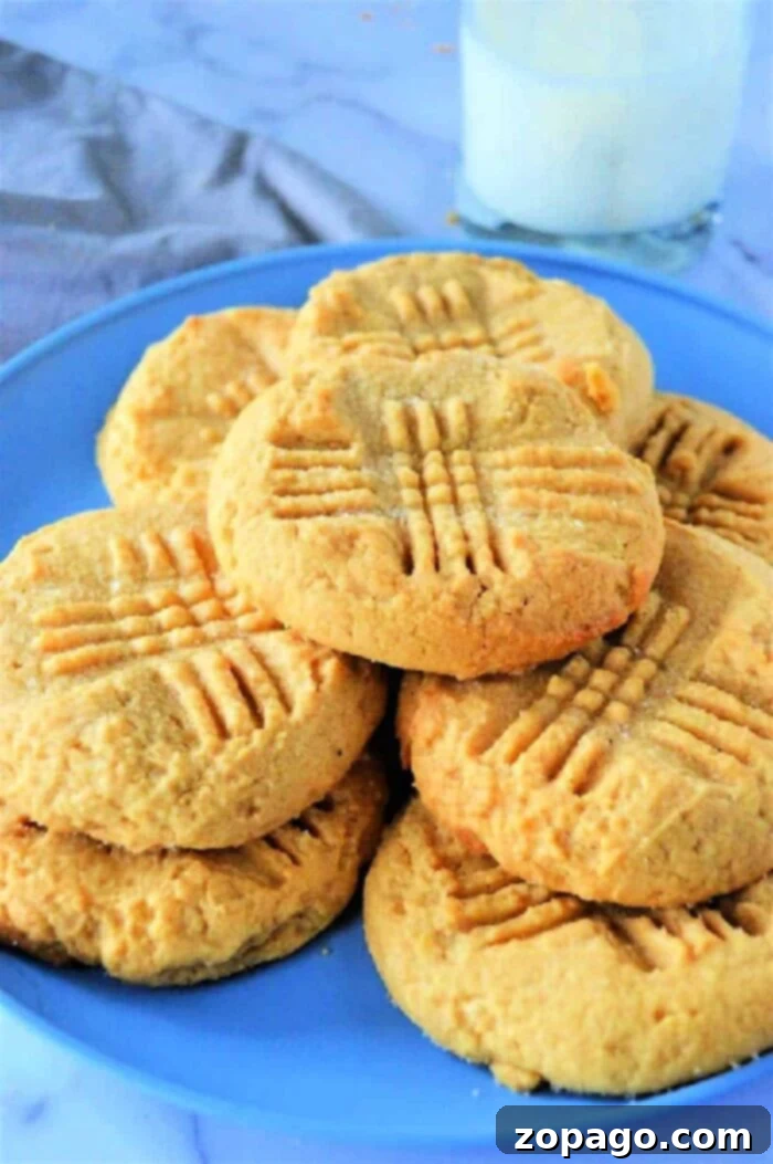 Effortless Cake Mix Cookies 2 A plate of golden-brown peanut butter cookies, made with cake mix, featuring classic crisscross fork marks, rests invitingly beside a tall glass of cold milk.