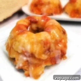 A Caramel Apple Bread Pudding mini bundt cake infused with the essence of caramel apple and finished with a luscious icing glaze, all elegantly displayed on a white plate.