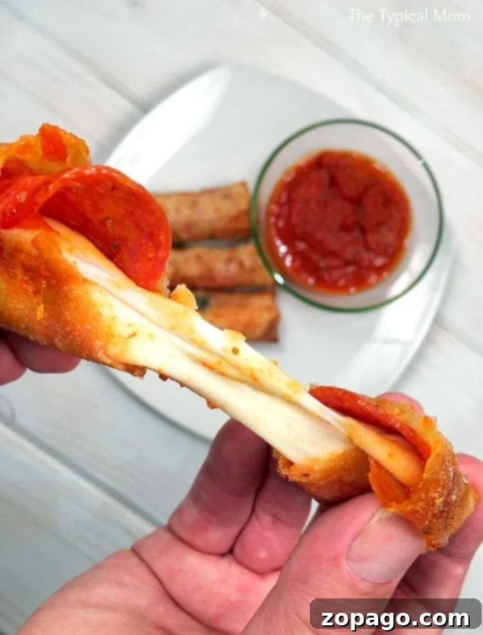 These pizza egg rolls are amazing!! They're so easy to make and your kids will love them right along with you too. It's a delicious appetizer made with all your favorite pizza toppings or a fun new dinner idea. Close-up of golden brown pizza egg rolls with melted cheese and pepperoni, served on a plate with marinara dipping sauce.