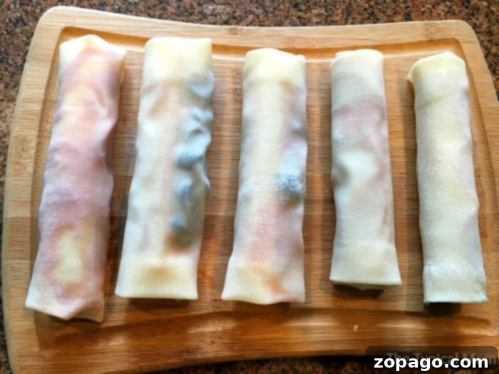 Crispy Pizza Bites 7 Five perfectly rolled, uncooked pizza egg rolls lined up neatly on a rustic wooden cutting board, showcasing uniform preparation before they are cooked to a golden crisp.