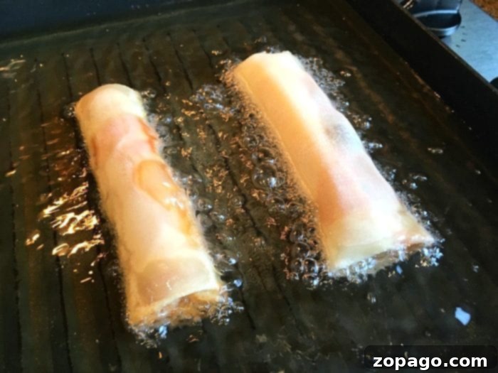 Crispy Pizza Bites 8 A close-up of a hand skillfully rolling an egg roll wrapper, meticulously sealing the edges to create a perfect pizza egg roll, with more prepared rolls visible in the background.