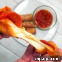A hand pulls a stringy, cheesy pizza egg roll from a pile, with marinara sauce in the background.