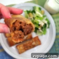 Close-up of a half-eaten sloppy joe egg roll held above a plate with more egg rolls and a Caesar salad.