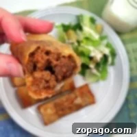 Close-up of a half-eaten sloppy joe egg roll held above a plate with more egg rolls and a Caesar salad.