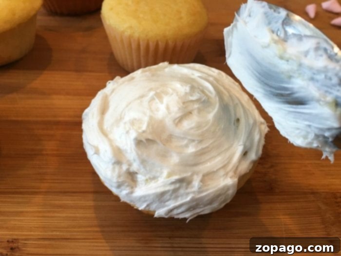 Fluffy Lamb Cupcakes 3 A cupcake being decorated with white frosting and mini marshmallow pieces to create the wool texture for a sheep cupcake, shown with additional candies and marshmallow slices for ears and eyes.