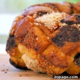 Close-up of a savory monkey bread loaf, elegantly braided and topped with sesame and poppy seeds, resting on a rustic wooden surface.