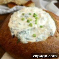 A round loaf of bread is hollowed out and generously filled with cold spinach dip, then topped with chopped green onions for a refreshing twist.