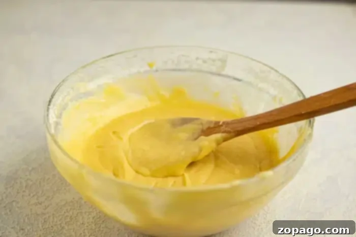 Perfectly portioned cake batter for a small batch of 6 cupcakes. A glass bowl filled with vibrant yellow cake batter, a wooden spoon resting inside, capturing the essence of preparing a small batch of delicious cupcakes.