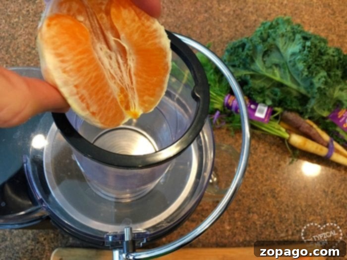 Easy Homemade Kale Juice 6 A hand squeezes an orange into a juicer, while kale and carrots sit in the background on a countertop, ready to inspire easy kale recipes.