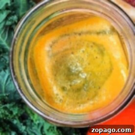 Top view of a glass of orange juice surrounded by fresh ingredients—kale, apples, carrots, and vibrant purple carrots—perfect for easy kale recipes.