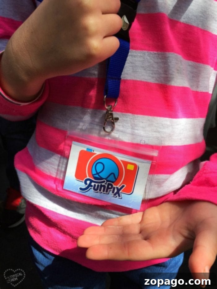 Knott's Berry Farm Photo Memories 2 A child in a striped pink shirt holds an empty plastic badge holder attached to a lanyard featuring the Knott's Berry Farm FunPix logo in vibrant colors, symbolizing easy access to digital memories.
