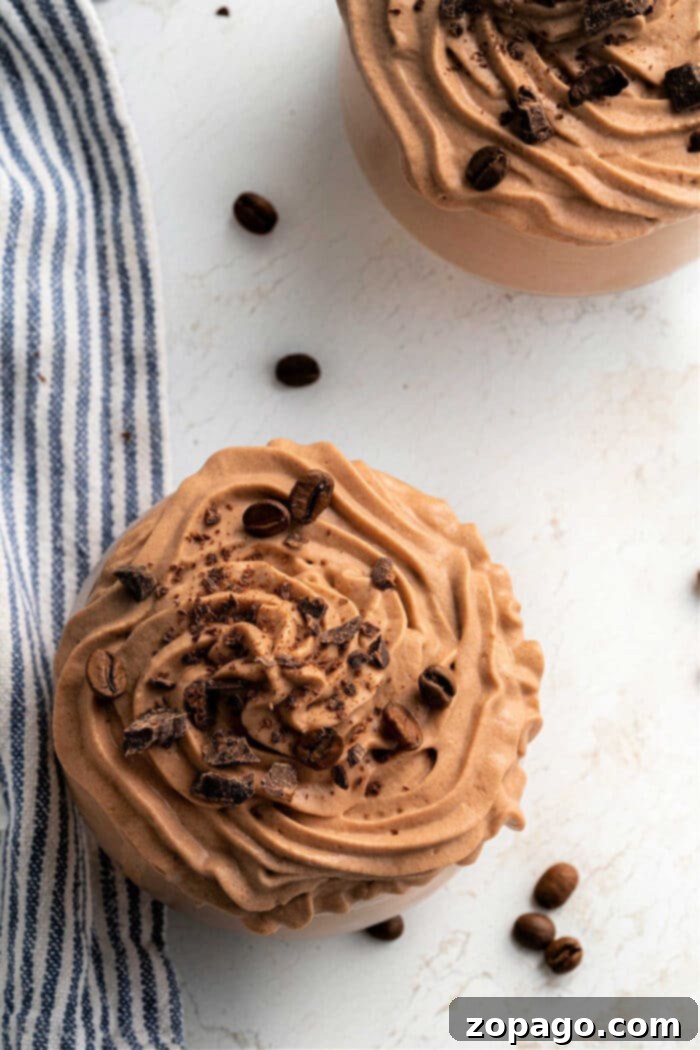Java Frosting 6 Two bowls of creamy chocolate coffee frosting, topped with cocoa nibs and coffee beans, on a white surface alongside a striped cloth.