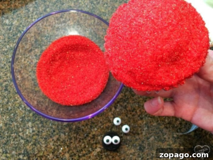 Whip Up Cute Ladybug Cupcakes 2 Hands dipping a red frosted cupcake into red sanding sugar to create a shiny finish.