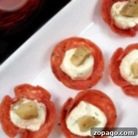 Salami cups filled with creamy cheese and topped with artichoke pieces sit beautifully arranged on a white plate, showcasing a delicious and easy appetizer recipe.