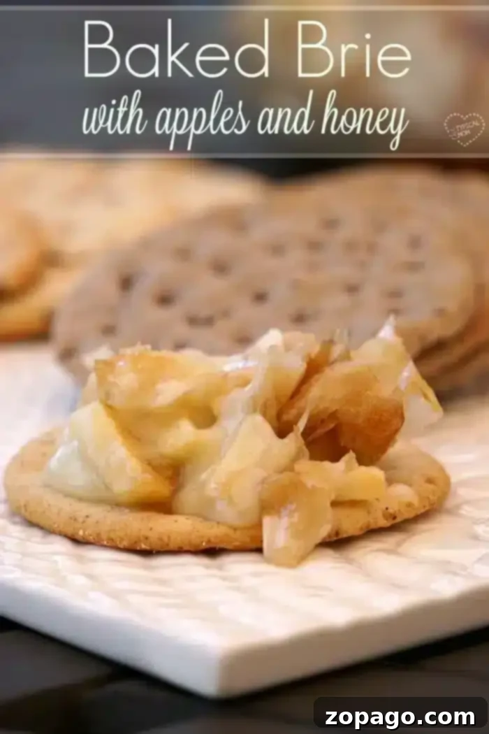 Flaky Baked Brie 7 A cracker topped with easy baked Brie cheese, apple pieces, and honey sits on a white plate. Blurred crackers appear in the background. The text