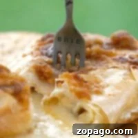 A fork labeled BRIE in melted brie cheese with a flaky phyllo dough crust rests on a wooden board.